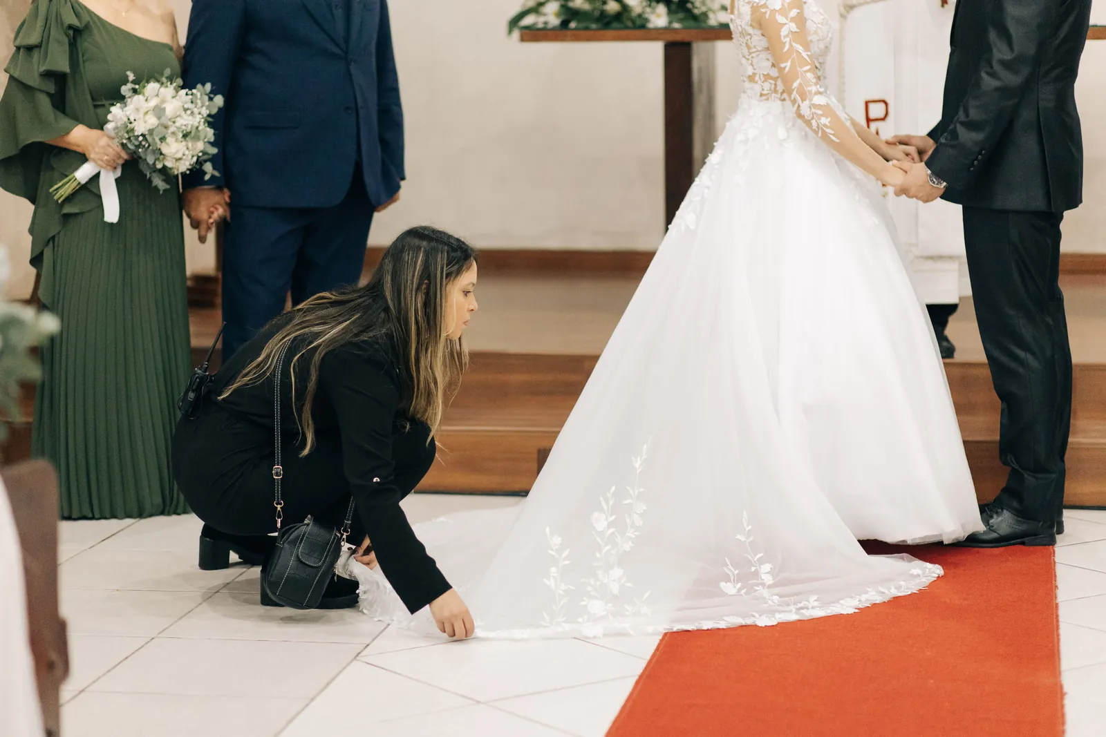 Camila ajeitando a cauda do vestido da noiva no altar
