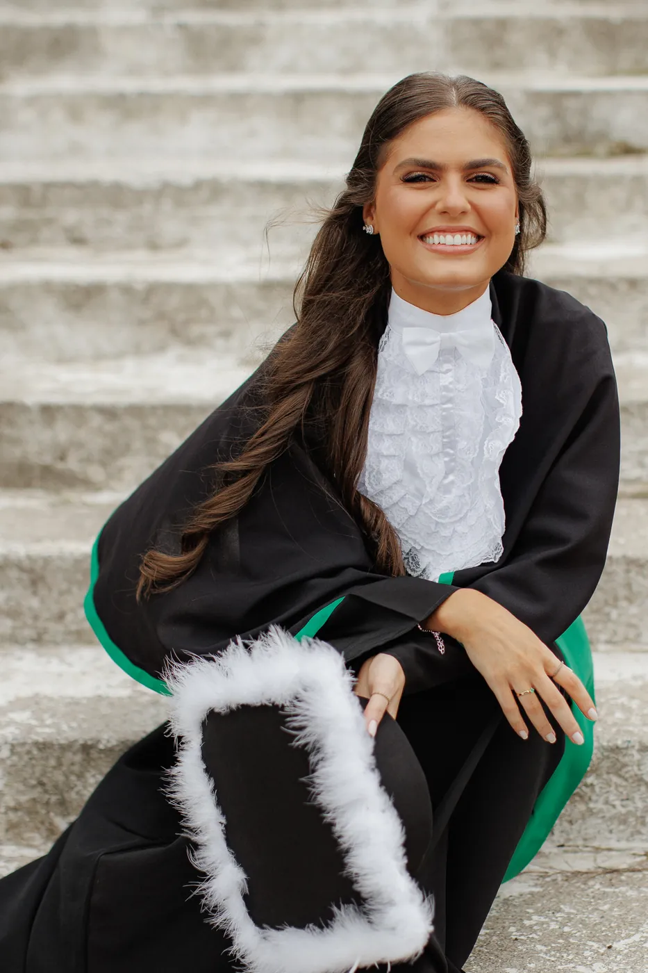 Formatura: formanda de beca sorrindo numa escadaria